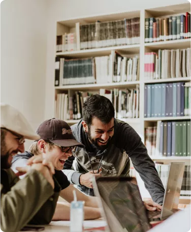Drei Männer arbeiten an Laptops in einer Bibliothek.