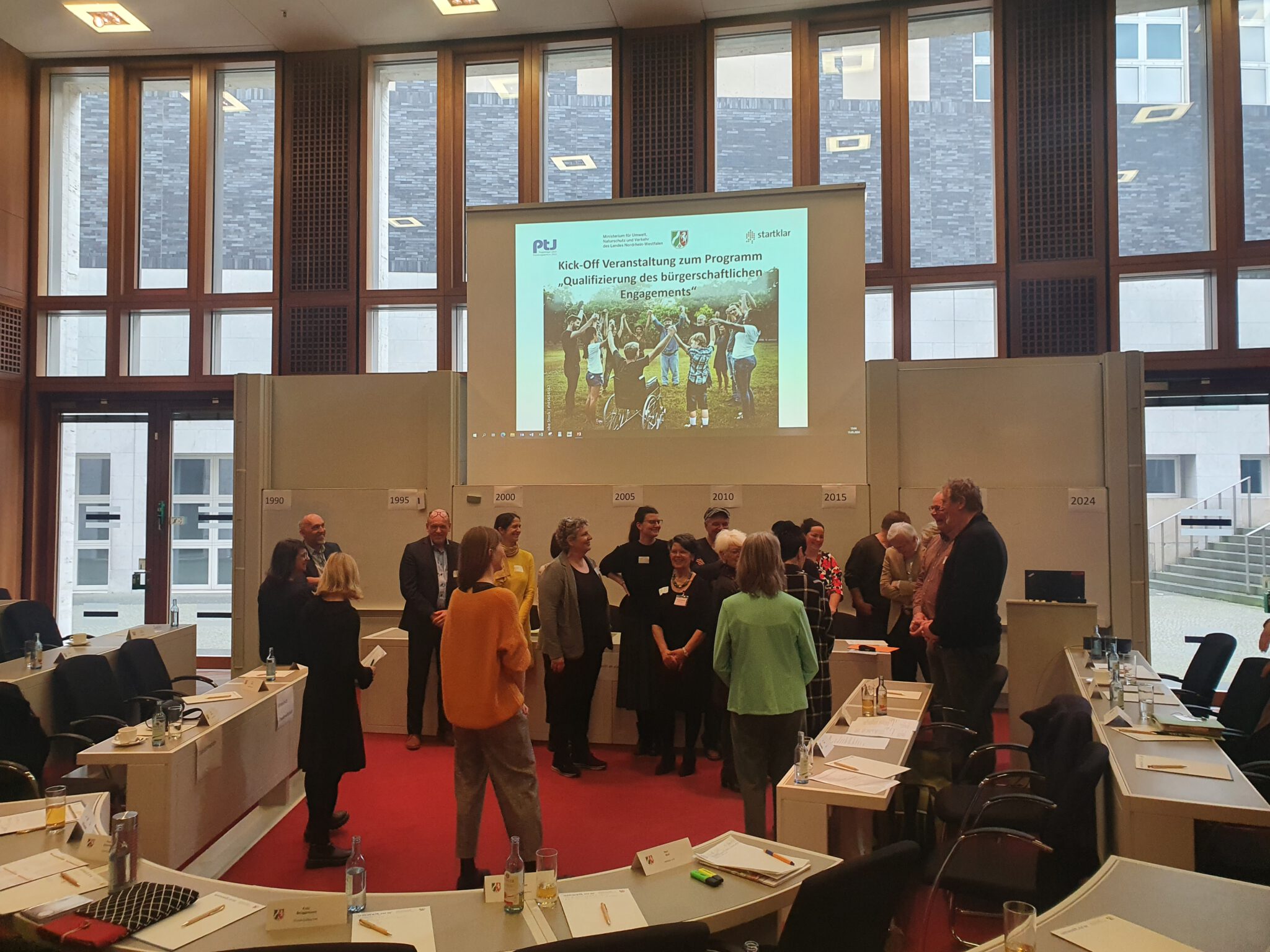 kickoff-2048×1536 Menschen stehen vorne an der Beamer-Wand in einem Veranstaltungsraum während eines Kickoff-Meetings